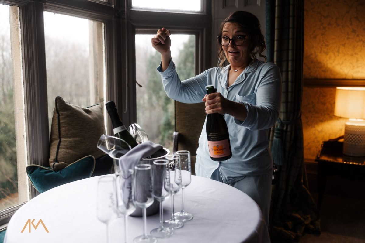 bride popping a bottle of Champagne Mitton Hall Winter Wedding